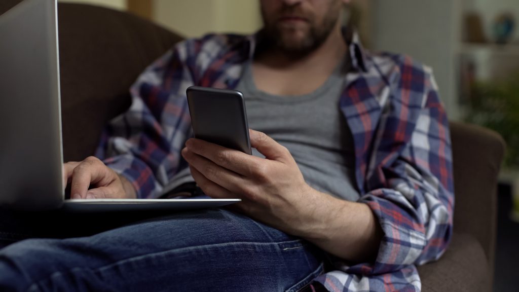 Men looking at phone while using a laptop