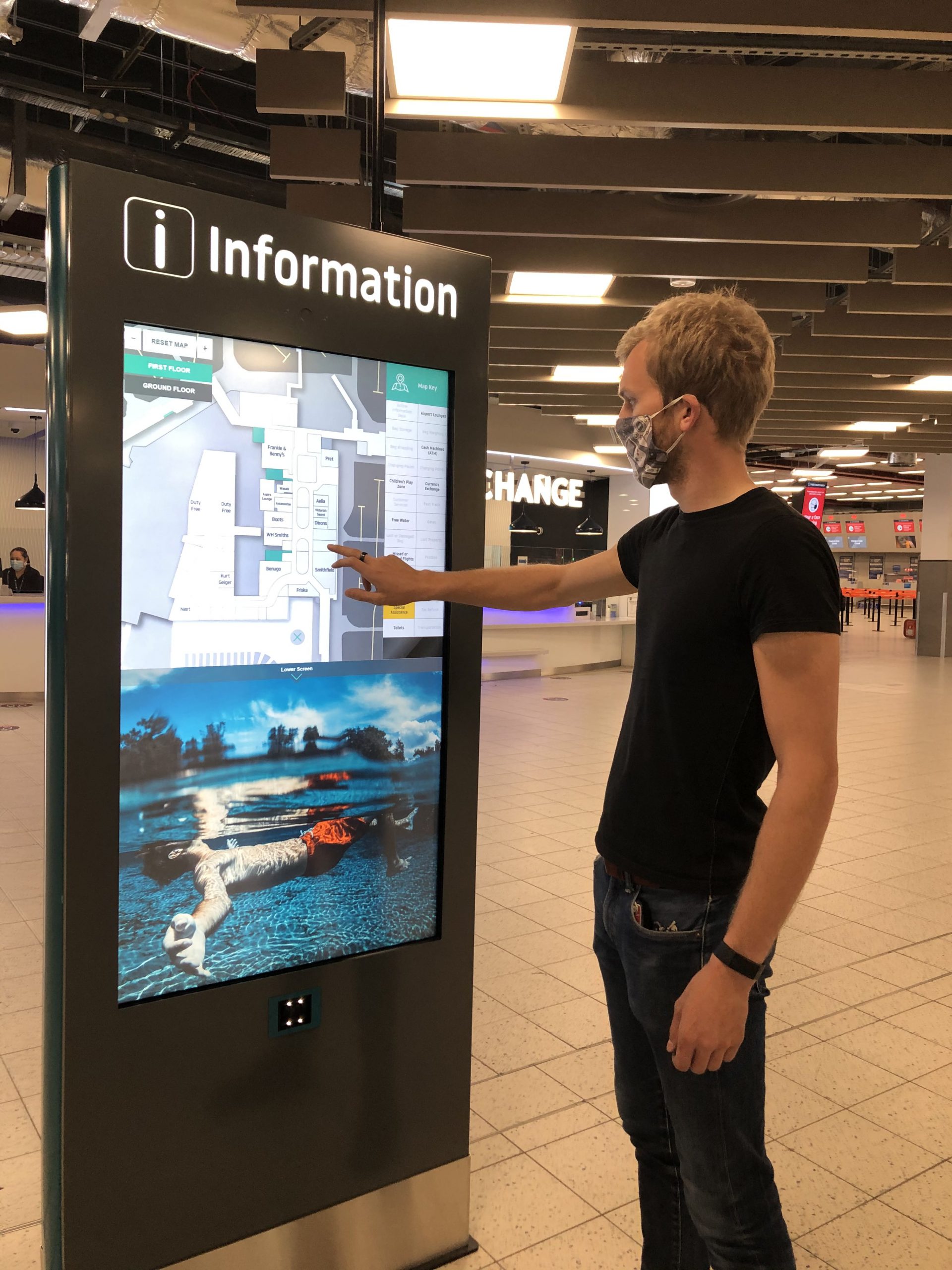 Young men wearing a face mask while interacting with the wayfinding totem at London Luton Airport